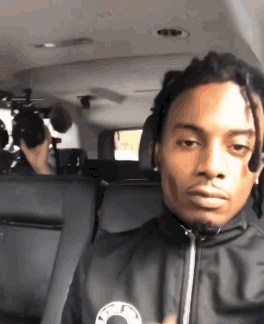 a man with dreadlocks is sitting in the back seat of a car with a camera behind him .