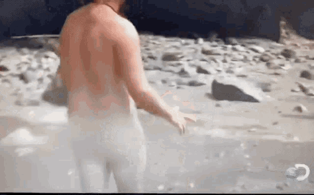 a naked man is walking on a beach in a video .