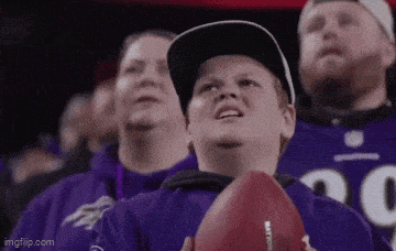a young boy is holding a football in a crowd of people .