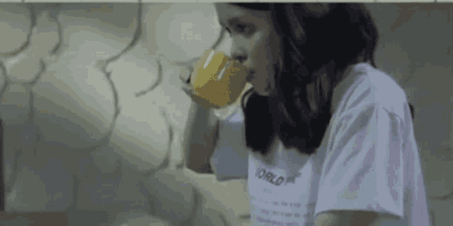 a woman is drinking a cup of coffee from a yellow mug .