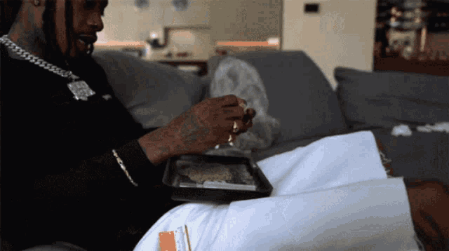a man sitting on a couch with a tray of weed in his lap