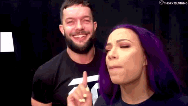 a man with a beard and a woman with purple hair are standing next to each other .