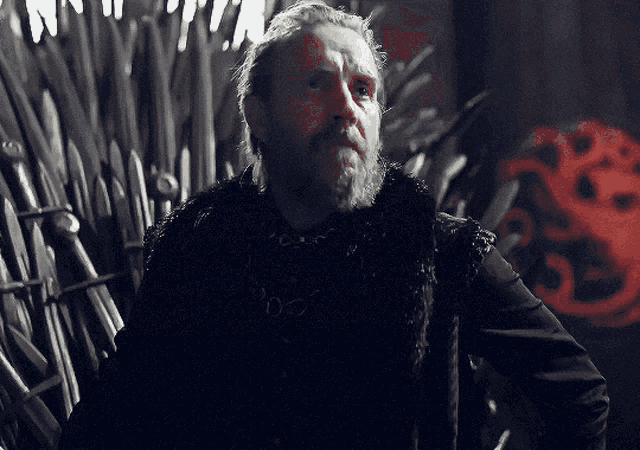 a man with a beard is standing in front of a throne with a red dragon on it