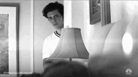 a black and white photo of a man standing in front of a lamp .
