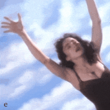 a woman with her arms outstretched against a blue sky with the letter e next to her
