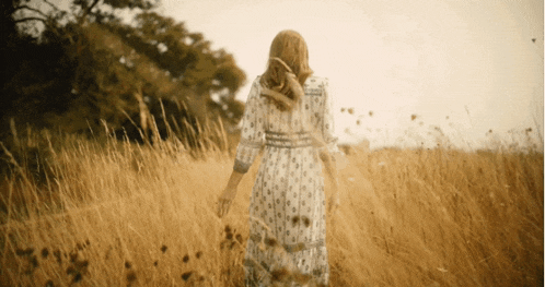 a woman in a dress is walking through a field