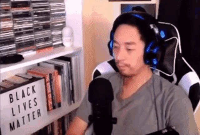 a man wearing headphones is sitting in front of a microphone in front of a sign that says " black lives matter "