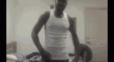 a man in a white tank top is standing in front of a bed