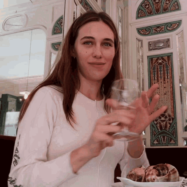 a woman in a white sweater holds a glass of wine in her hand