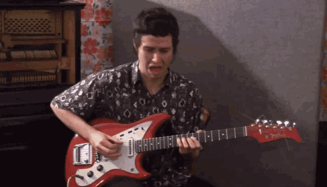 a man is playing a red fender guitar in front of a piano