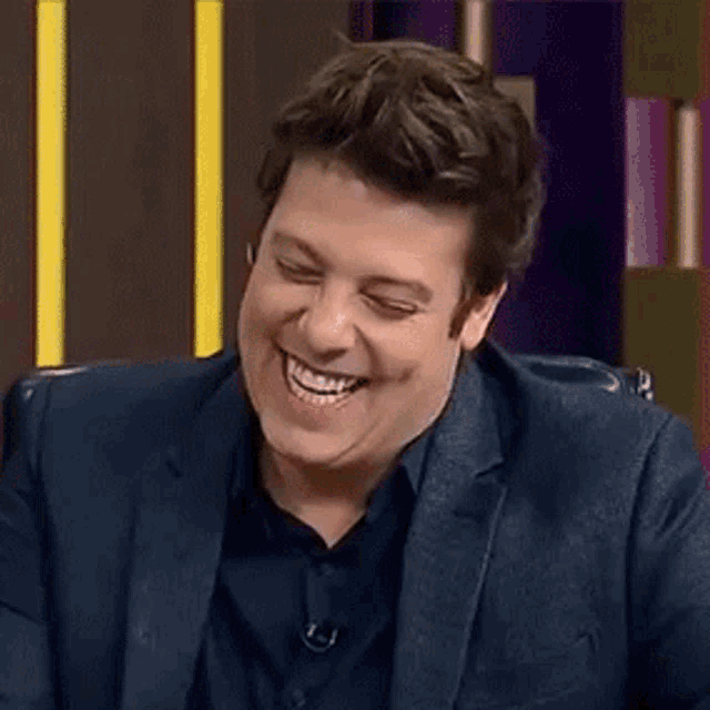 a man in a suit and black shirt is laughing and smiling .