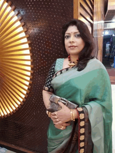 a woman in a green saree holds a purse