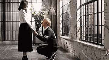 a man is kneeling down to kiss a woman in a room with a brick wall .