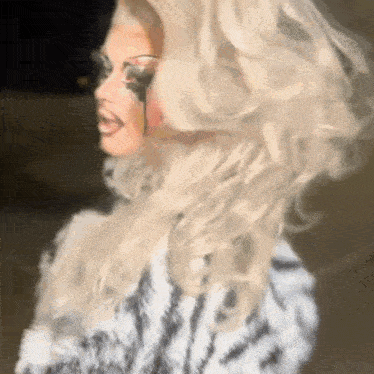a drag queen with blonde hair and a zebra print coat is standing in front of a black background .