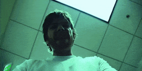 a man in a white shirt is standing in a dark room with a green light on the ceiling .