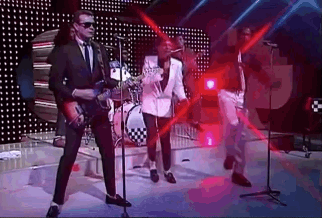 a man in a suit is playing a guitar in front of a microphone