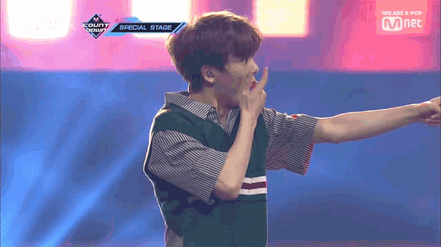a man in a green vest stands on a stage in front of a mnet banner
