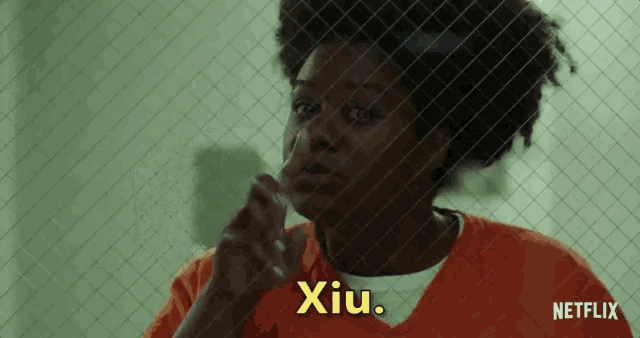 a woman in an orange prison uniform is behind a chain link fence and says xiu .