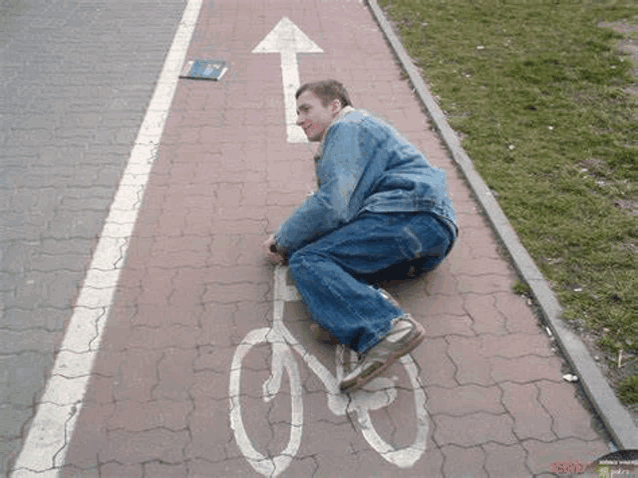 a man is kneeling on a brick sidewalk next to a bicycle lane .
