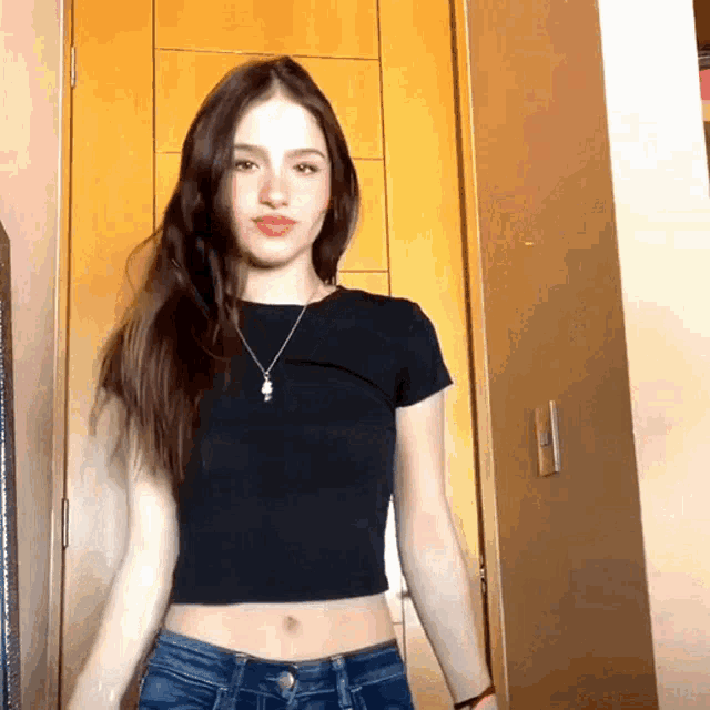 a woman wearing a black crop top and jeans stands in front of a door
