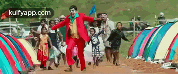 a man in a clown costume is running with a group of children in front of tents .
