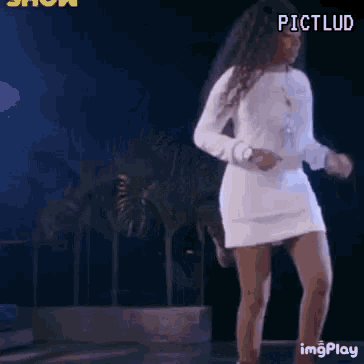 a woman in a white dress is dancing on a stage in front of palm trees .