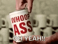 a person is holding a can of whoop ass oh yeah .
