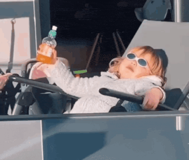 a little girl wearing sunglasses is sitting in a stroller holding a bottle of water .