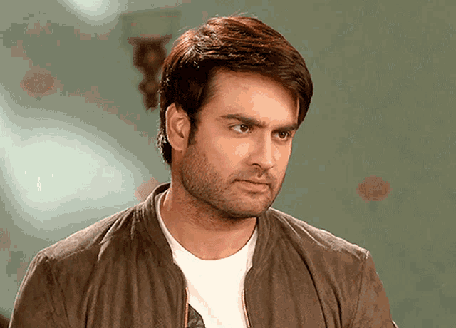 a man with a beard wearing a brown jacket and white shirt