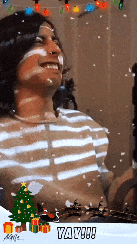 a man in a striped shirt is smiling in front of a christmas tree with the words yay !!! below him