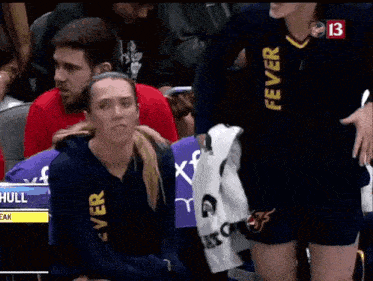 a woman wearing a fever jersey sits in the stands during a basketball game