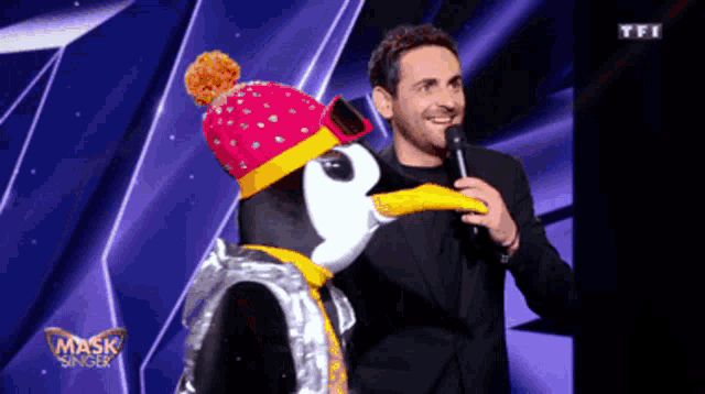 a man in a suit stands next to a masked penguin on a stage