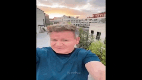 a man in a blue shirt is taking a selfie on a balcony .
