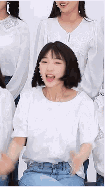 a girl with short hair is sitting in front of a group of girls wearing white shirts and blue jeans .