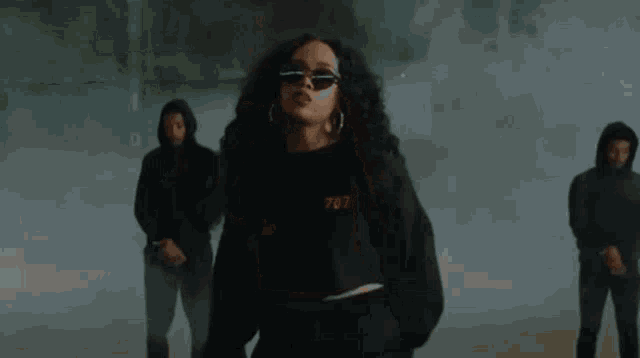 a woman wearing sunglasses and a black sweater is dancing in front of a group of men .