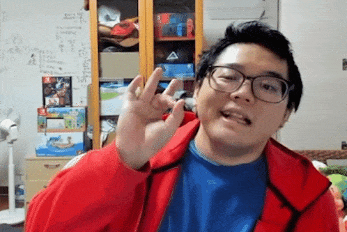 a man wearing glasses and a red jacket is giving a peace sign