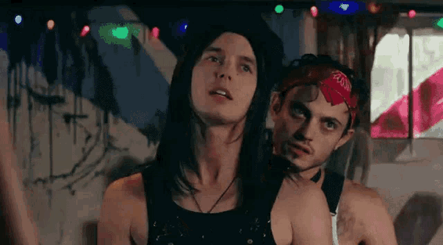two men are standing next to each other in a room with christmas lights on the wall .