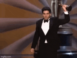 a man in a tuxedo is holding an oscar trophy in front of a statue .