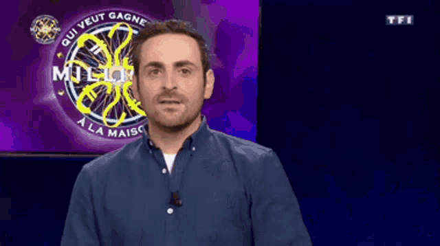 a man in a blue shirt is standing in front of a who wants to be a millionaire sign