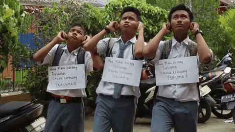 three boys covering their ears while holding signs that say " aku mau datang "