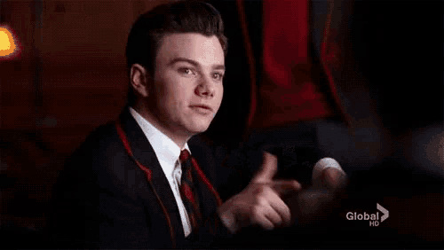 a man in a suit and tie is giving a thumbs up while sitting at a table .