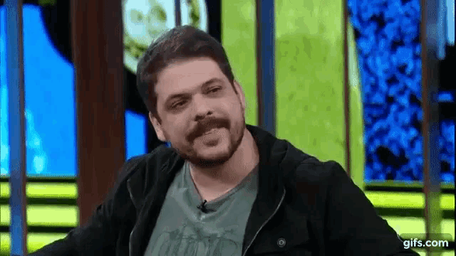 a man with a beard and mustache is smiling while sitting in front of a television screen .