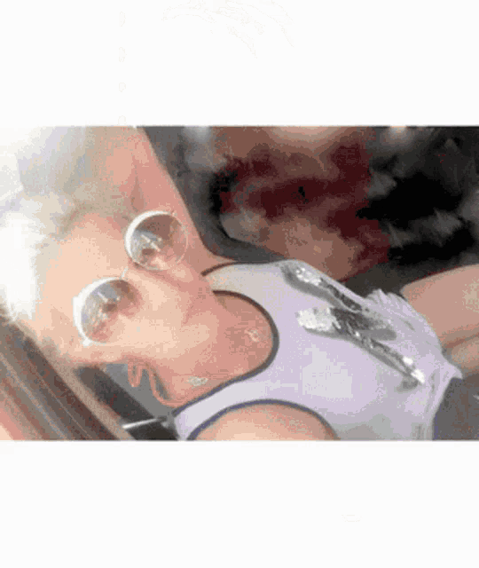 a woman wearing sunglasses and a purple tank top is laying down