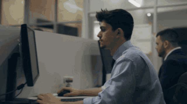 a man in a blue shirt sits at a desk in front of a computer monitor
