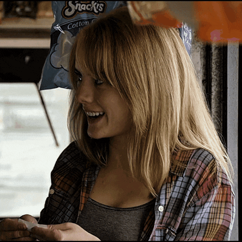 a woman in a plaid shirt is smiling in front of a bag of snacks cotton candy