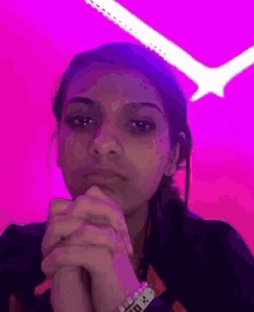 a woman is praying with her hands folded in front of a pink and purple background .