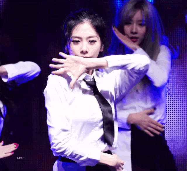 a woman in a white shirt and black tie is dancing in front of a screen that says ldc on it