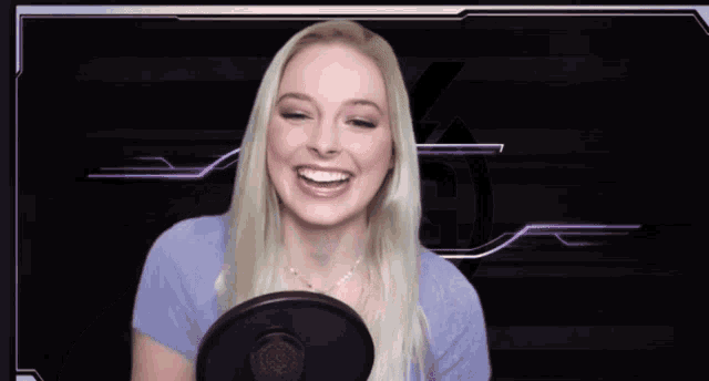 a woman is laughing in front of a microphone with a purple background