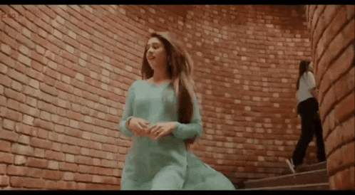 a woman in a blue dress is standing in front of a brick wall and stairs .