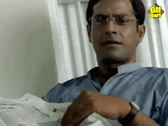 a man wearing glasses and a watch is reading a newspaper with a gif bar logo behind him